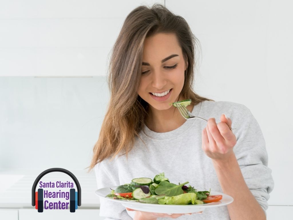 A woman holding a plate of vegetable salad and a fork looking down smiling.